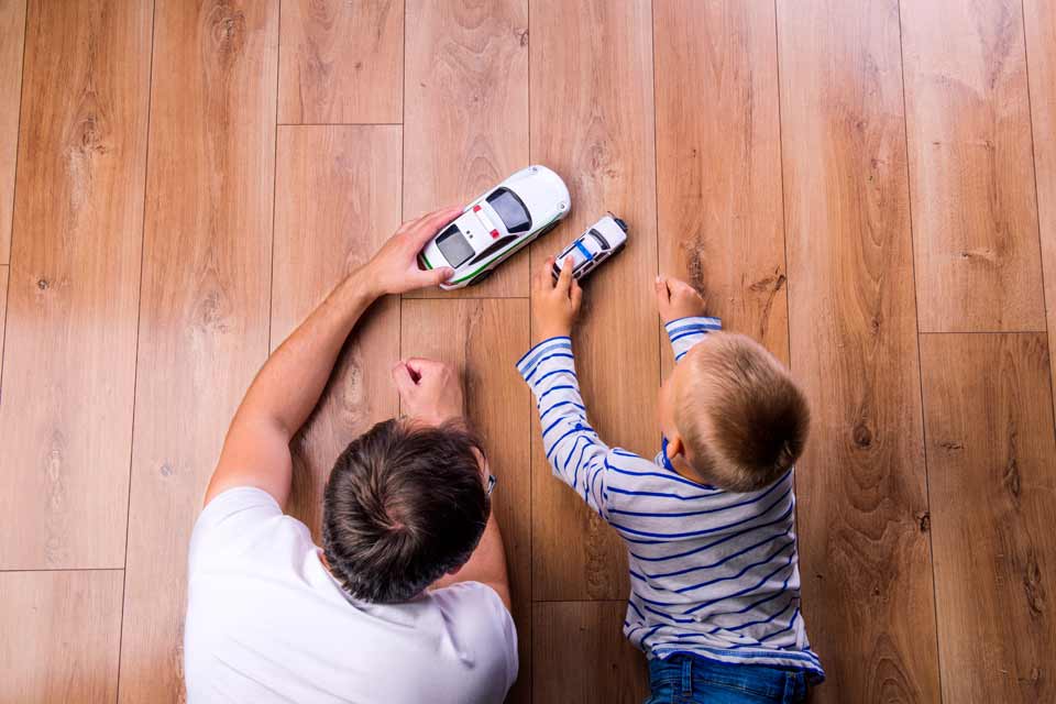 child and father playing on the floor with cars